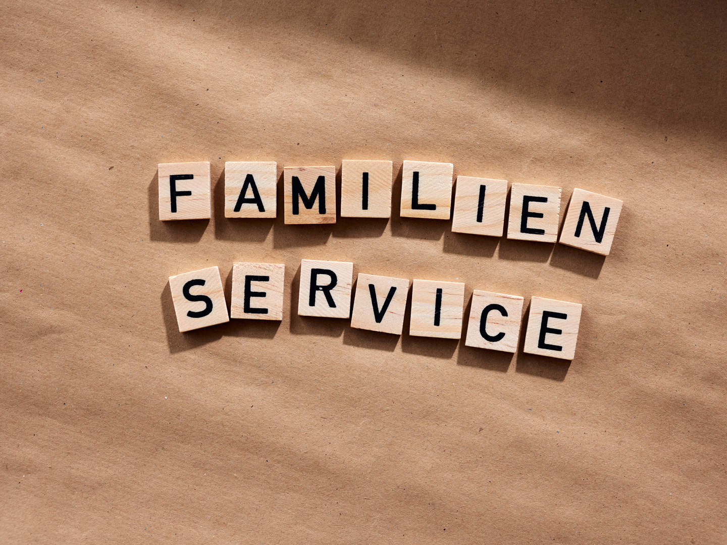 Holztfelchen mit Buchstaben liegen auf einem Tisch und zeigen den Schriftzug "Familien Service"